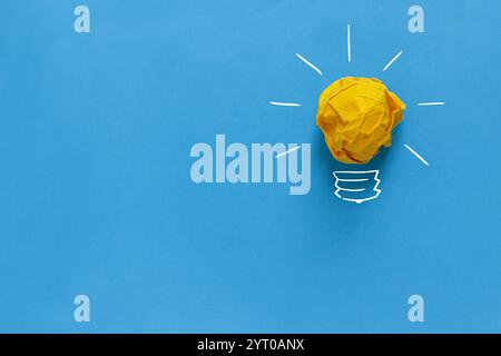 Inspiration concept crumpled paper light bulb metaphor for good idea. Yellow crumpled paper light bulb drawn on a blue background. Brainstorm and crea Stock Photo