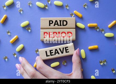 Paid Period Leave symbol. Concept words Paid Period Leave on wooden blocks. Beautiful purple background with pills. Doctor hand. Healthcare and Paid P Stock Photo