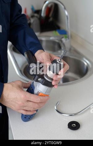 a caucasian man, wearing blue overalls, puts a metal drill bit in an electric drill before to drill a hole in a metal sink, to install a faucet, in th Stock Photo