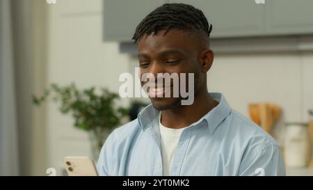 Happy smiling positive African American ethnic man user carefree male ethnic guy smile holding smartphone using mobile phone chatting social media Stock Photo