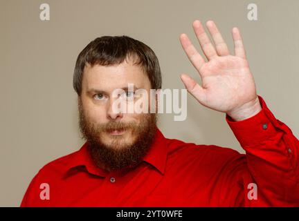 A man with a beard and red shirt waves his hand Stock Photo