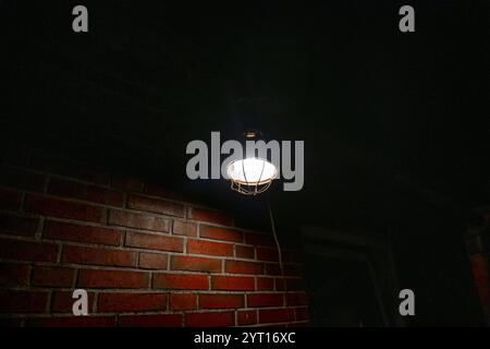 A warm light fixture hangs from the ceiling, casting a soft glow on a rustic brick wall. The atmosphere is moody and evocative, showcasing an industri Stock Photo