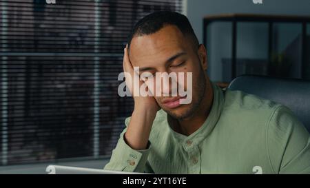 Tired lazy young african american businessman bored at work fall asleep at office desk sleepy overworked ethnic man employee sleeping at workplace Stock Photo