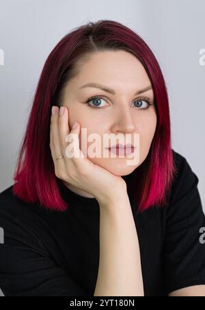 Portrait of a young woman with vibrant cherry red hair on a light background. Vertical crop. Close up. Stock Photo