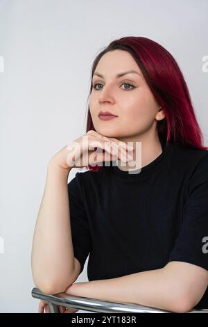 Portrait of a young woman with vibrant cherry red hair on a light background. Vertical crop. Close up. Stock Photo