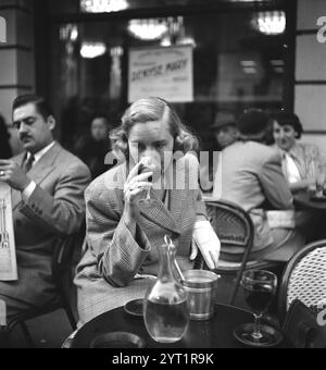 Woman dressed in a coat drinking red wine at a Parisian cafe. Paris, France, 1940s, from Life of a Marshall plan Secretary in Paris, DPLA, Stock Photo