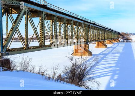 A bridge spans a river with snow on the ground. The bridge is made of metal and is very long Stock Photo