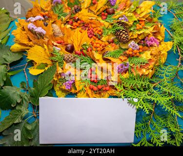 A vibrant arrangement features fallen leaves in shades of gold and orange, mixed with colorful berries, pine cones, and small flowers on a blue surfac Stock Photo