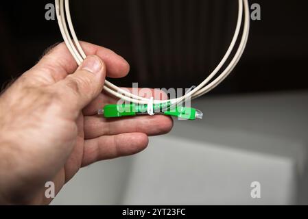 Close-up of a hand holding a coiled fiber optic patch cable with green SC APC connectors, ideal for high-speed internet and professional telecommunications setups Stock Photo