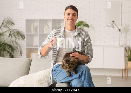 Young man with cute cat and cup of tea at home Stock Photo