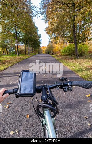 View from a bicycle handlebar on a paved path through a park with autumn trees. Stock Photo