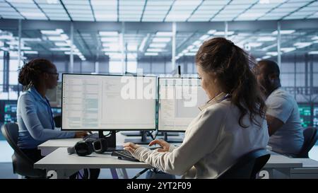 Smiling manager in server hub using computer to find firewall misconfigurations affecting rackmounts performance. Upbeat supervisor checking systems bottlenecks affecting data transfer rates, camera B Stock Photo