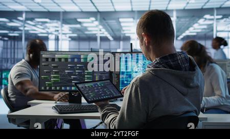 System administrator in data center solving tasks on tablet, running programming scripts. Software developer manipulating lines of code for AI applications development using device Stock Photo