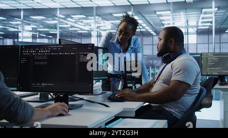 Engineer working with colleague on computer in high tech data center establishment monitoring hardware energy consumption. Team of technicians using PC to check for system failures, camera B Stock Photo