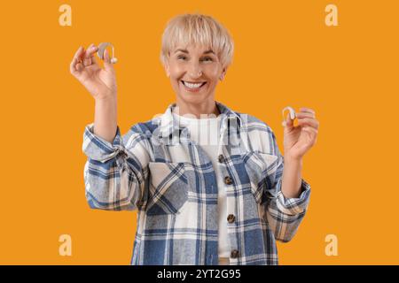 Mature woman with hearing aids on  yellow background Stock Photo