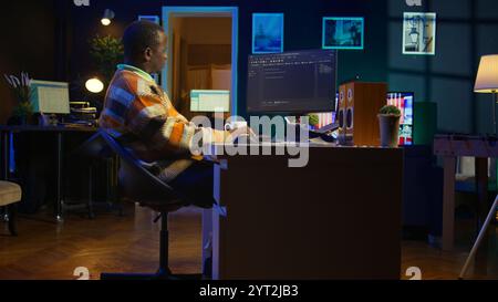 Programmer in home office concentrating on finding bugs while he codes on his computer. African american IT admin frowning while looking at screen, confused by errors in lines of code. Camera B. Stock Photo