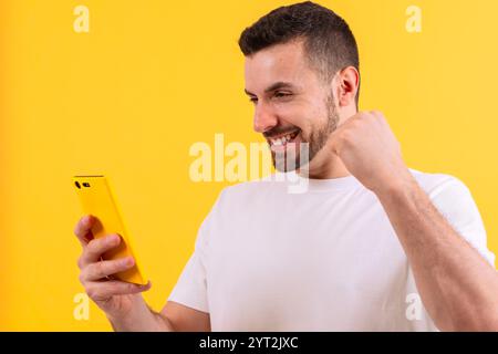 Excited man celebrating success while using smartphone on yellow background Stock Photo