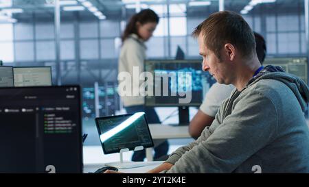 Technician arriving at work in high tech server room, analyzing data on monitors, ensuring seamless data flow. Man starting job shift in data center, ensuring system integrity and security, camera A Stock Photo