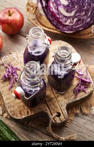 Three bottles of purple cabbage juice with fresh apples and cucumber on a table Stock Photo