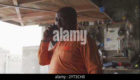 Front view of an African male owner of a panel beater workshop in a township, talking on the smartph Stock Photo