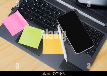 Wooden office table with pen, note papers and smartphone on laptop. Top view, copy space. Stock Photo