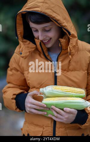 Boy in winter jacket holding several corn cobs in hands Stock Photo