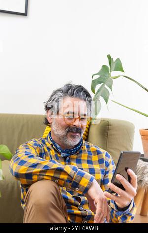 Smiling man using a smartphone sitting in his living room Stock Photo