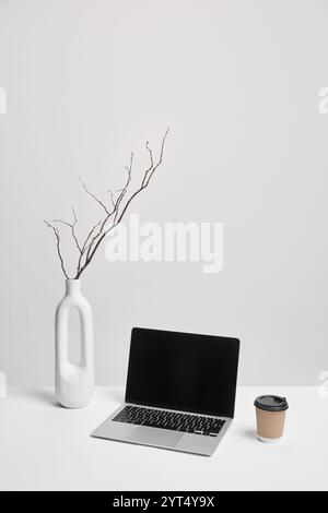 Laptop, coffee cup, and white vase on clean desk. Balanced composition with room for overlays. Ideal for marketing or business mockups. Stock Photo