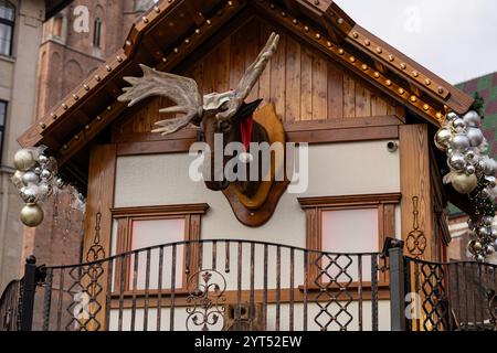 Wooden chalet at the Wroclaw Christmas Market featuring a decorative moose head in a Santa hat, adorned with silver ornaments and fairy lights Stock Photo
