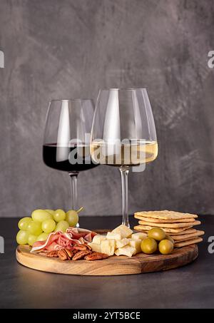 Food photography of red and white wine, cheese parmesan, prosciutto, olives, pecan, grapes, crackers, wine glasses, assortment, party meal, romantic d Stock Photo