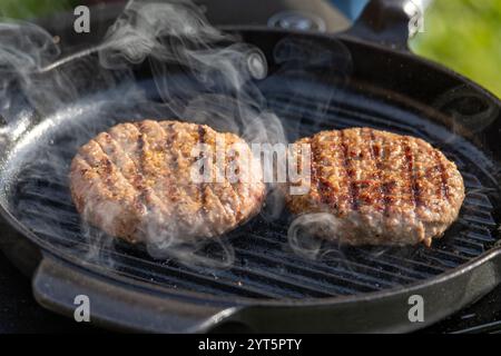fresh burger meat patty grilling on grill pan in the garden Stock Photo