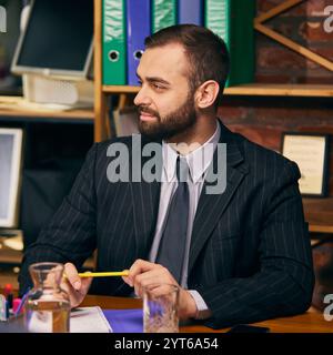 Bearded young businessman attentively listening to colleagues during business meeting, holding pen and taking notes. Stock Photo