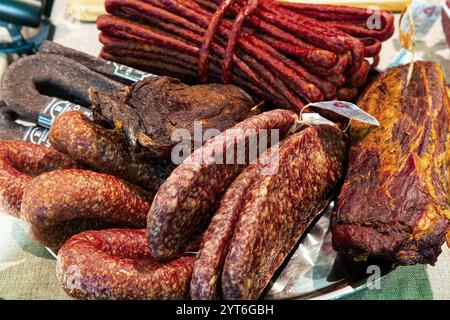 Various delicious jerky gammon and sausages on dish, top view. Traditional ready-to-eat meat products on the counter in the market. Stock Photo