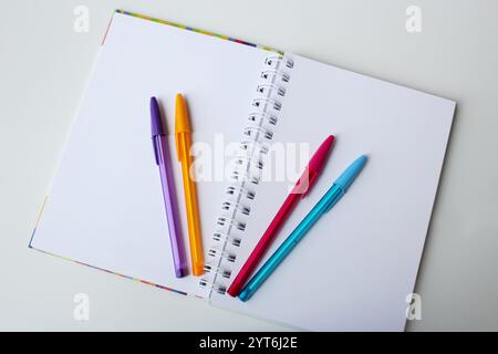 Blank page paper notebook on white background with four color pens. Creative stationery, office supplies, art lesson, back to school concept. Stock Photo