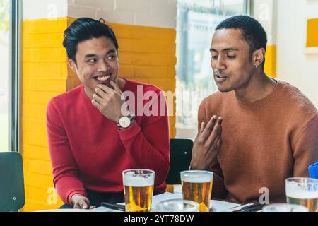 Two diverse businessmen enjoying a beer together while discussing work at a cafe table Stock Photo