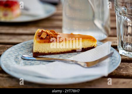 Caramel cake on plate with napkin and fork, jug with fruit water drink, glass and second plate with strawberry cake on table. Stock Photo