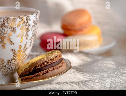 luxurious scene featuring a gold-trimmed teacup paired with a chocolate macaron accented in gold leaf, surrounded by colorful macarons on a soft, text Stock Photo