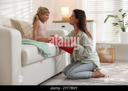 Mother helping her daughter to put tights on at home Stock Photo