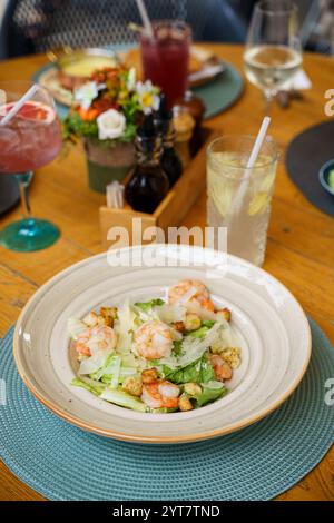 A fresh Caesar salad topped with grilled shrimp, shaved Parmesan, and golden croutons served in a rustic bowl. A refreshing gin and tonic garnished wi Stock Photo