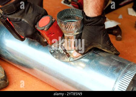 Technical worker in gloves works on attaching metal duct components with using power tool in during maintenance HVAC heating systems Stock Photo