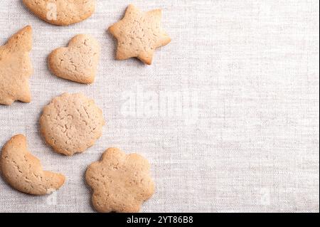 Homemade gingerbread cookies of different shapes on linen fabric, with empty space for text. Sweet, light brown and flat baked goods for Christmas. Stock Photo