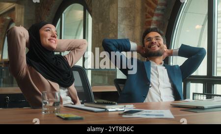 Businessman businesswoman male female working laptop writing notes at office two business colleagues Muslim woman in hijab Indian man finish complete Stock Photo