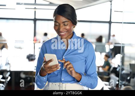 Smiling African American business woman using smartphone standing in office. Stock Photo