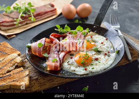 Crispy fried eggs with fried pancetta strips served rustic in an iron pan Stock Photo