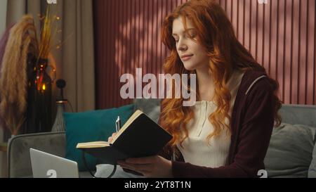 Caucasian woman at home writing notes drink coffee working from home student girl online studying e-learning homework write notebook exam tasks female Stock Photo