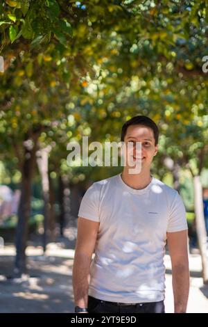 Young man in casual summer attire walking along a tree-lined path in Malaga's Mediterranean garden, with dappled sunlight creating natural patterns. Stock Photo