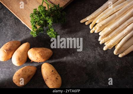 Fresh white asparagus and potatoes on black background. Spring vegetables on modern black kitchen plate. Seasonal gastronomy concept. Stock Photo