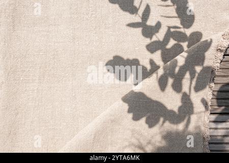 Natural textile background with plants shadows in sunlight. Draped beige linen fabric on wooden table with space for text. Background for weddings in boho style. Stock Photo