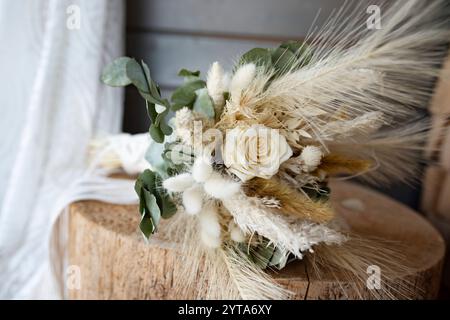 Beatyful dried bridal bouquet in natural boho style on rustic wood. Sustainable wedding decoration. Floral still life with wedding dress. Stock Photo