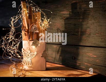 Handmade advent calendar made of cardboard. Small cardboard boxes in a paper bag decorated with a string of lights on rustic wooden background. Eco friendly christmas packaging. Background for a christmas greeting card. Stock Photo